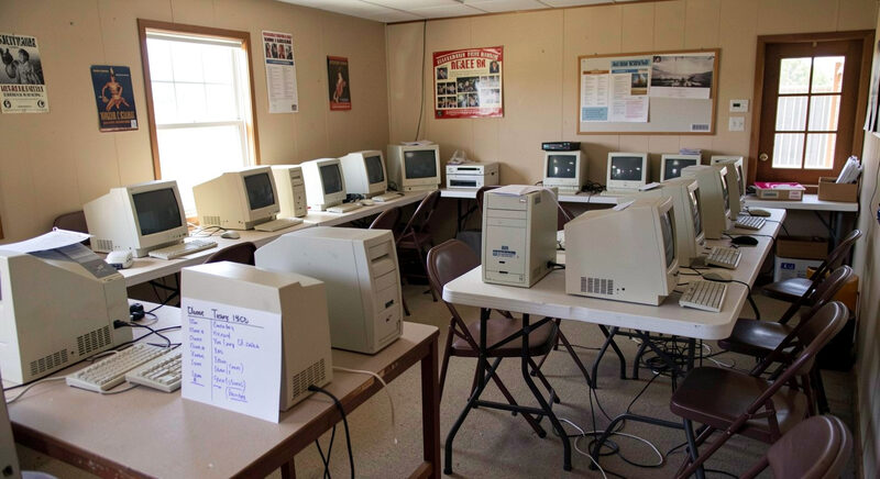 A volunteer-run community computer room in 1990s Texas with donated PCs, folding chairs and a handwritten sign-up sheet.